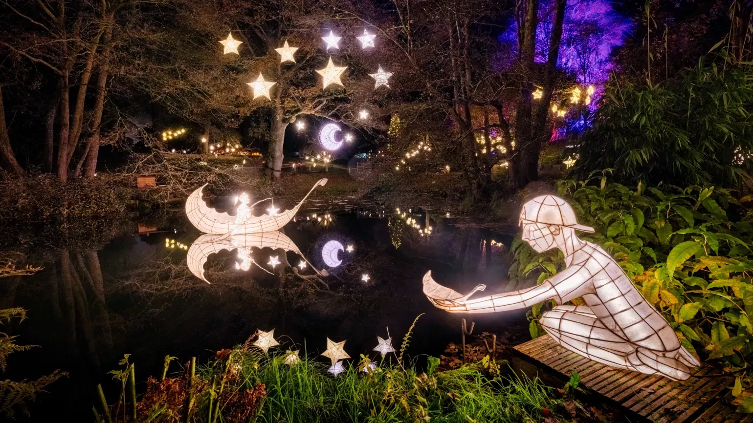 Lanterns over a lake at Glow Wild 2023, Jim Holden © RBG Kew Moon, stars, boat and boy lanterns on a lake at Wakehurst