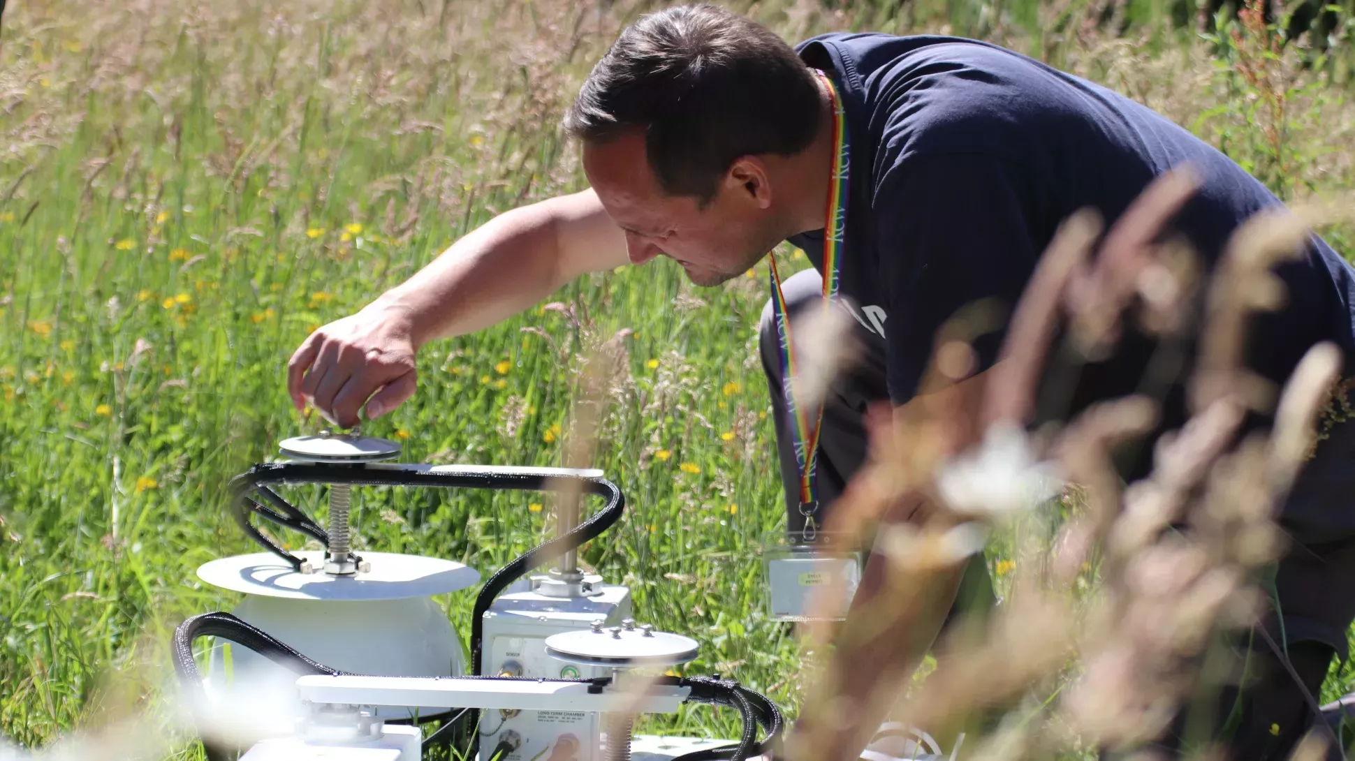 Dr Gary Egan sets up his permanent monitoring chambers © RBG Kew A person adjust pieces of white scientific equipment in a field of grass