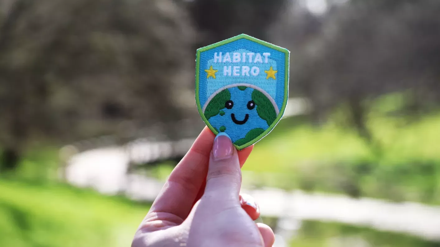 Habitat hero badge © RBG Kew Close up of a blue and green embroidered badge featuring a smiling planet Earth and the words Habitat Hero