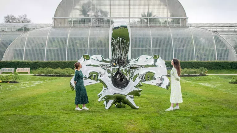 Marc Quinn at Kew, Ines Stuart-Davidson © RBG Kew A pair of people look at a shiny metal orchid sculpture in front of the palm house at 澳洲幸运8手机彩票开奖网