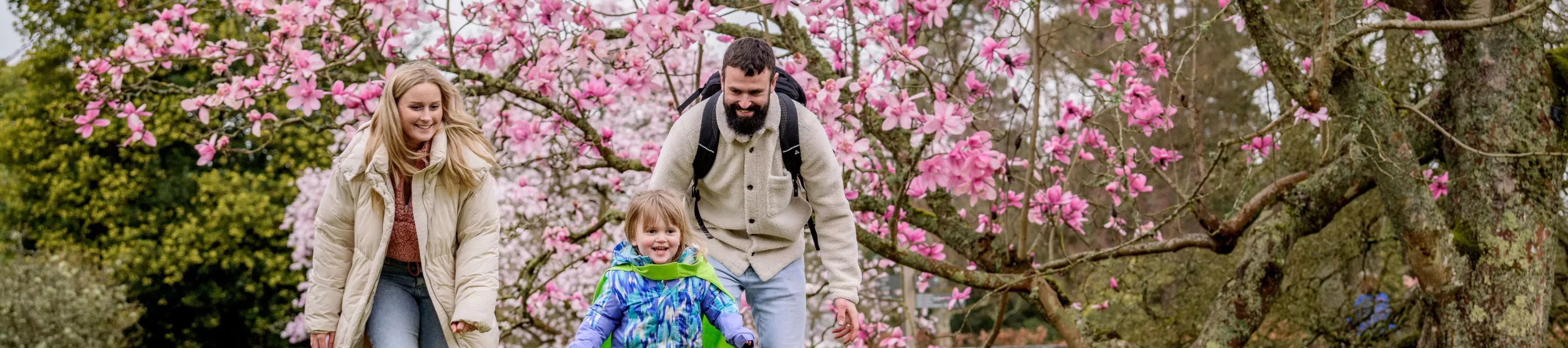 Wakehurst in spring © RBG Kew A family outdoors in front of a pink magnolia tree in full bloom